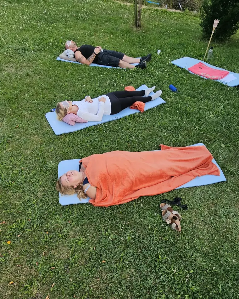 Teilnehmende einer Breathwork Journey liegen im Freien entspannt auf Matten im Gras